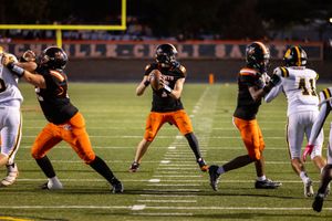 Offensive line in orange uniforms protects quarterback during nighttime football game.