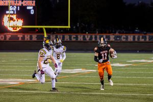 Player in orange jersey runs with ball while being chased by defenders at night.