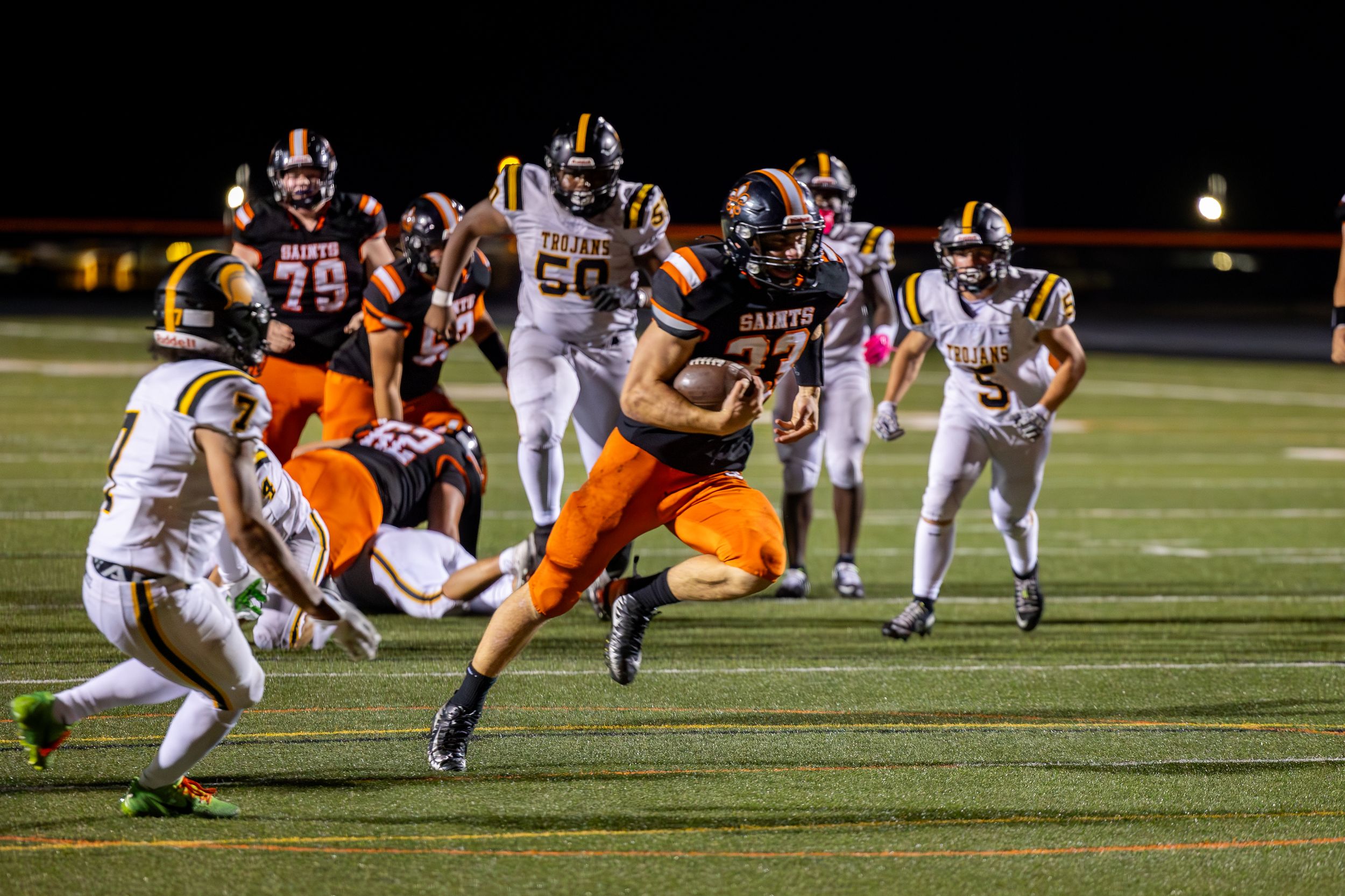 Football player in orange jersey leaps through defenders during night game action.