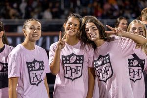 Group wearing matching pink shirts poses together at sporting event.