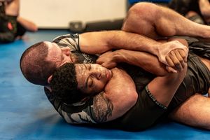 Two wrestlers grappling on blue mat during intense match.