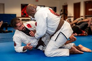 Brazilian Jiu-Jitsu practitioners sparring on mat wearing white gis.