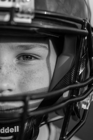 Close-up black and white photo showing football player's eye through helmet facemask.