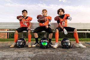 Group of football players sitting on ground in orange uniforms during team photo.