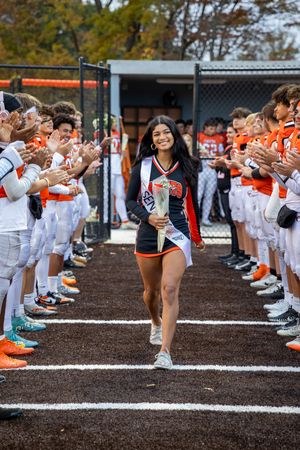Student athletes form a spirit tunnel in orange and white uniforms as someone walks through during a special ceremony.