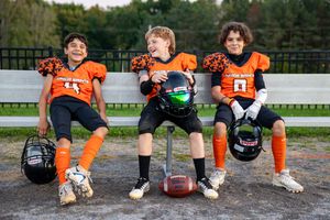 Youth football players in orange jerseys sitting together on ground for team photo.