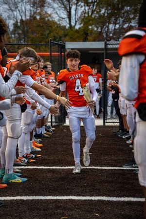 Football player in orange jersey runs through teammates forming a spirit tunnel on the field.