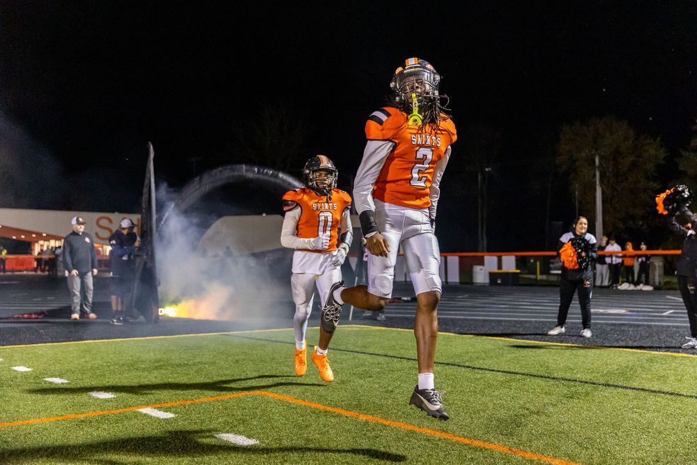Two football players celebrate on the field at night with smoke effects in the background.