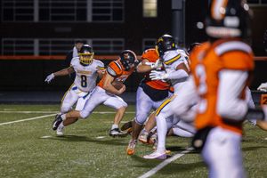 High school football game action shot showing offensive and defensive players mid-play.