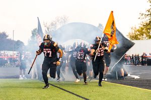 Football team runs through smoke onto field during dramatic game entrance.