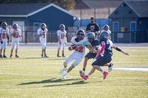 Youth football players in blue and white uniforms diving for a tackle on the field.