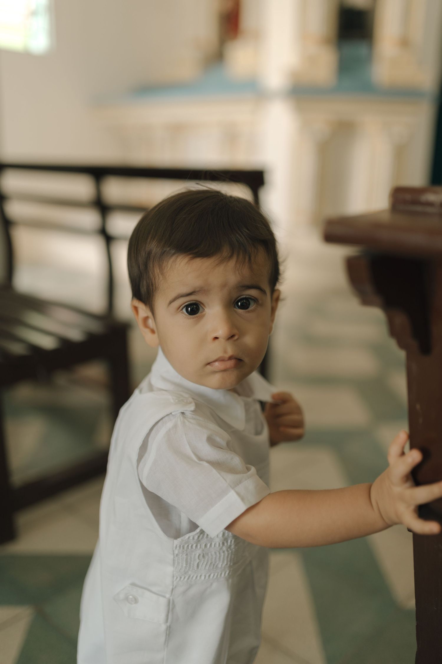 A small child in white clothing touches a wooden pew inside a church.