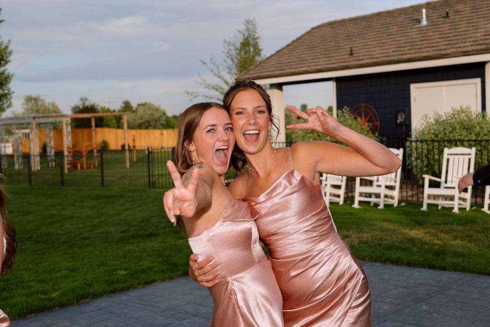 A group of bridesmaids in pink satin dresses pose together outdoors at a rustic countryside wedding venue.