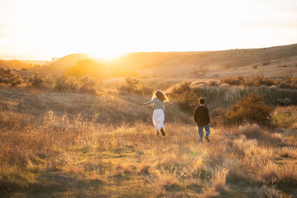A couple walks hand in hand through a golden field at sunset creating a romantic silhouette against the warm sky.