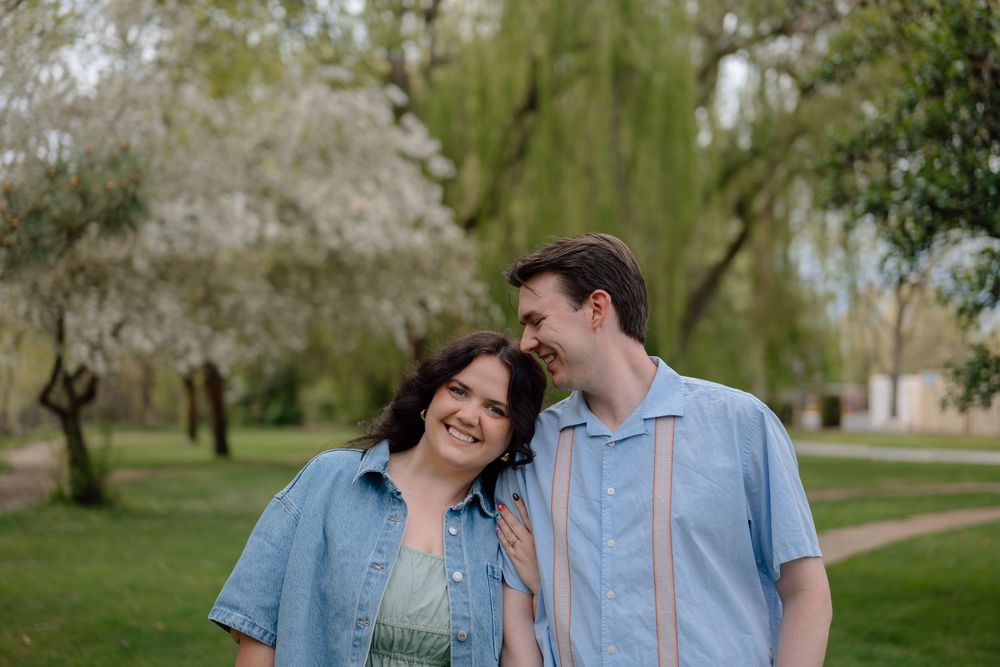 A couple in blue outfits walks together through a spring park with blooming trees in the background.