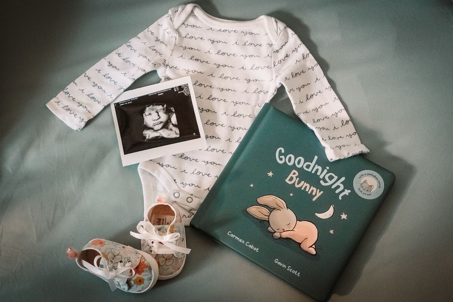 Baby announcement flat lay with onesie, children's book, sonogram and tiny shoes.