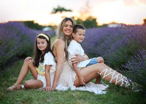 A mother and two children sit together smiling in a purple lavender field at sunset.