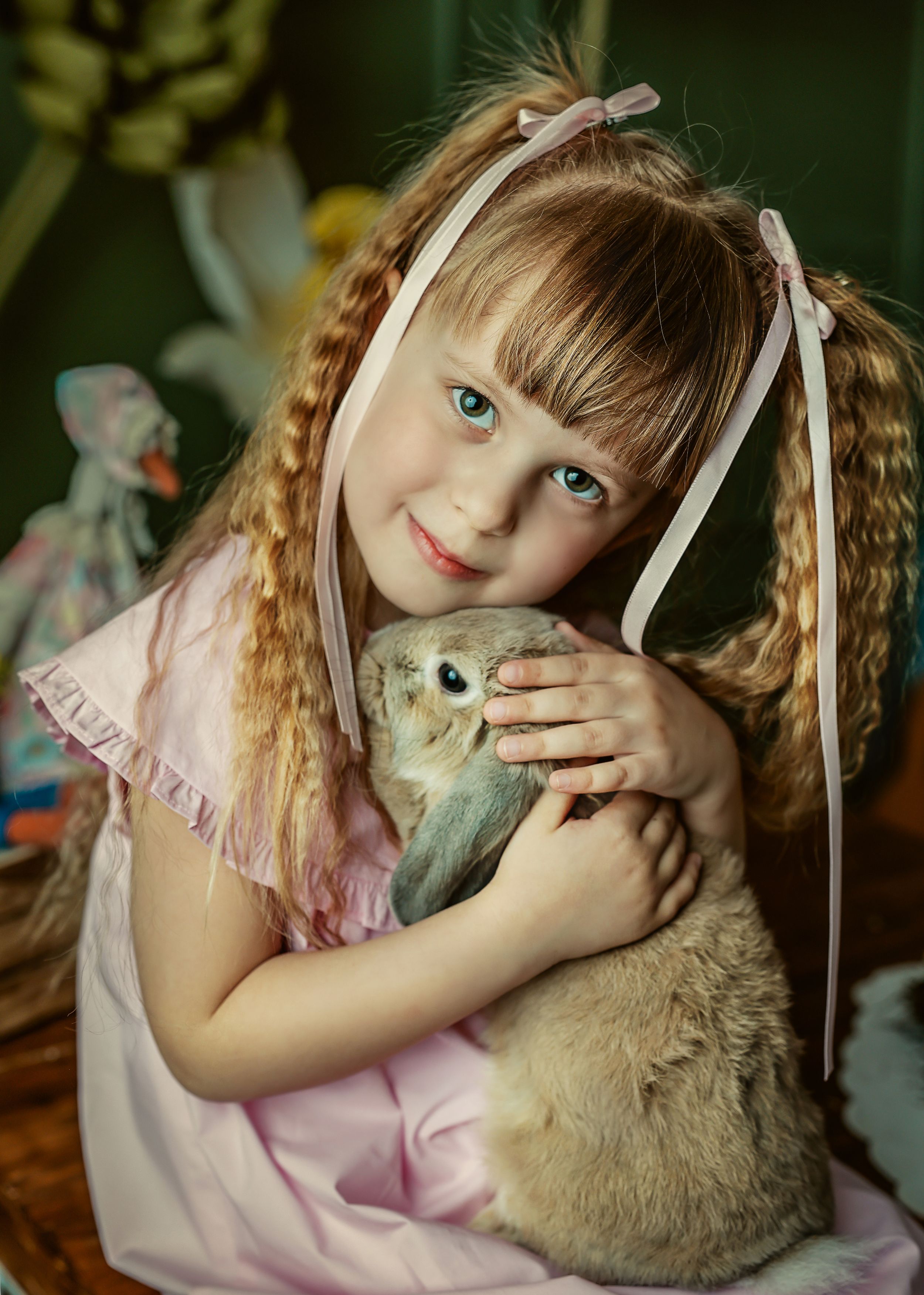 Blue-eyed girl with braids and pink bows hugs a fluffy rabbit in a pink dress.