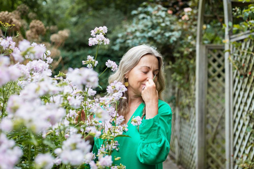 A person in a bright green shirt stands among blooming spring flowers in a garden setting.