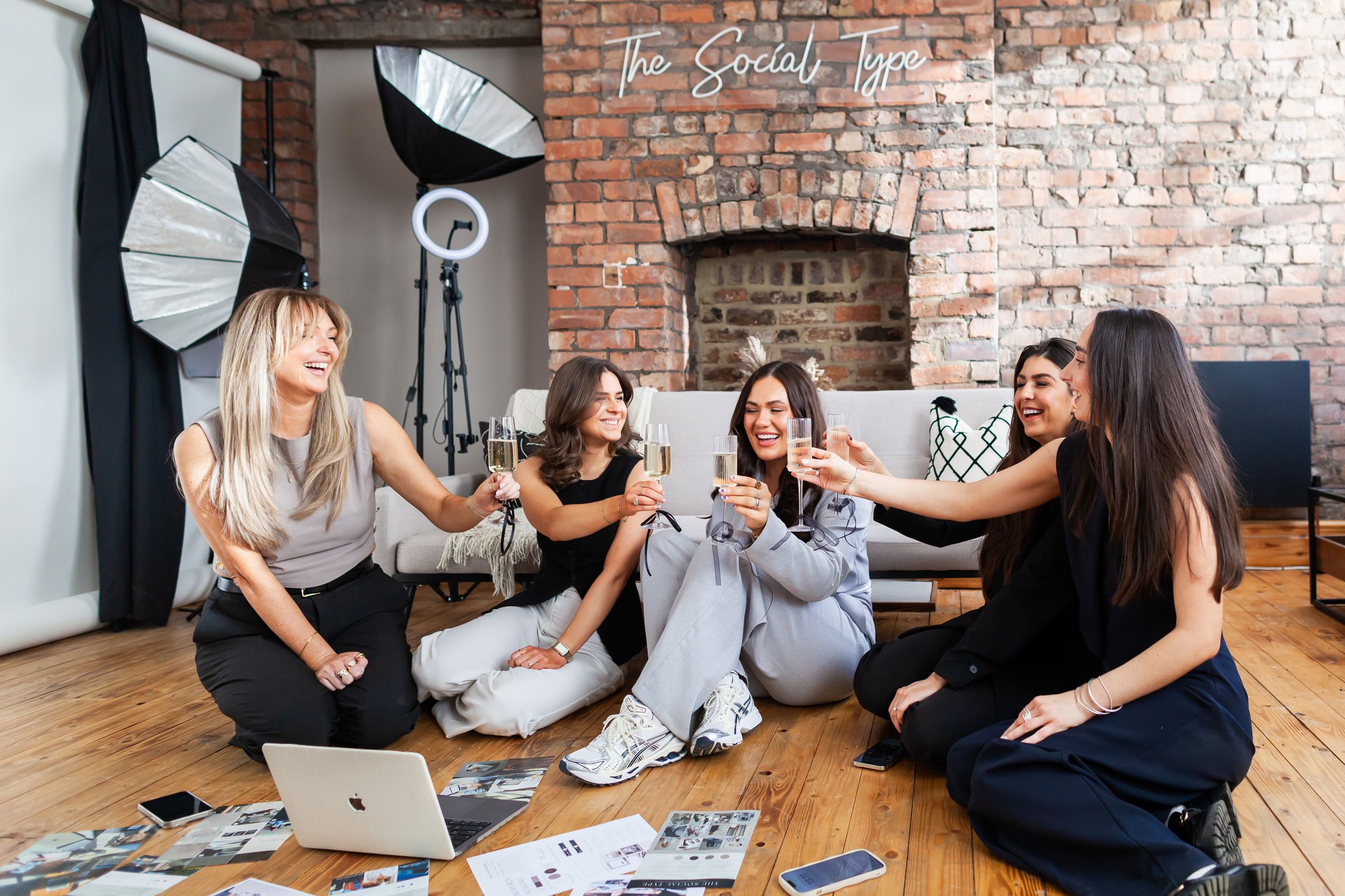 Group of women sitting on wooden floor in casual setting having animated conversation and laughing together.
