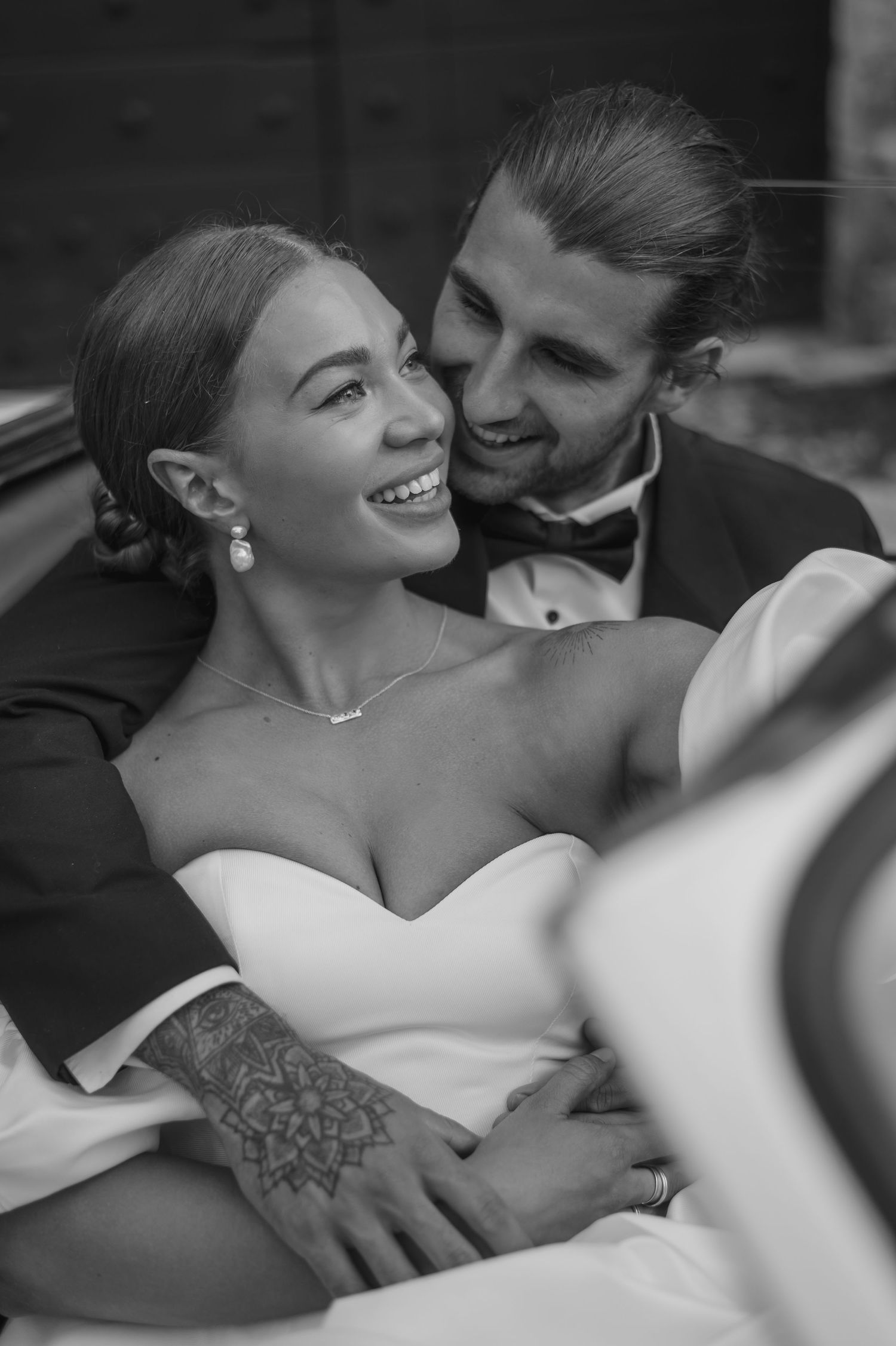 Black and white romantic wedding photo of couple embracing and laughing together in formal attire.