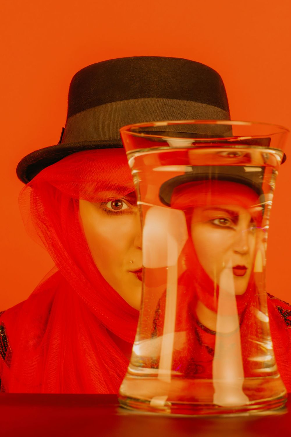 Creative portrait through glass with red lighting and hat creating distorted reflections.