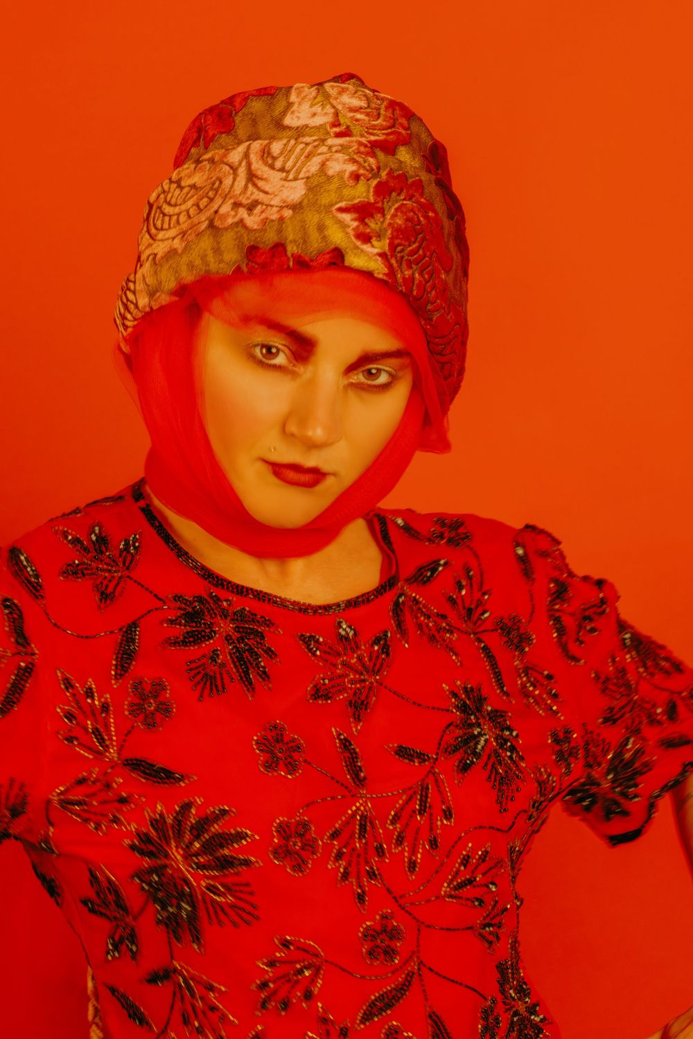 Portrait with dramatic red lighting wearing patterned clothing and ornate headpiece.