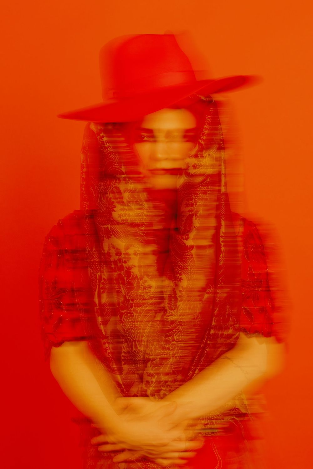 Silhouetted figure in hat captured in motion against vibrant orange background.