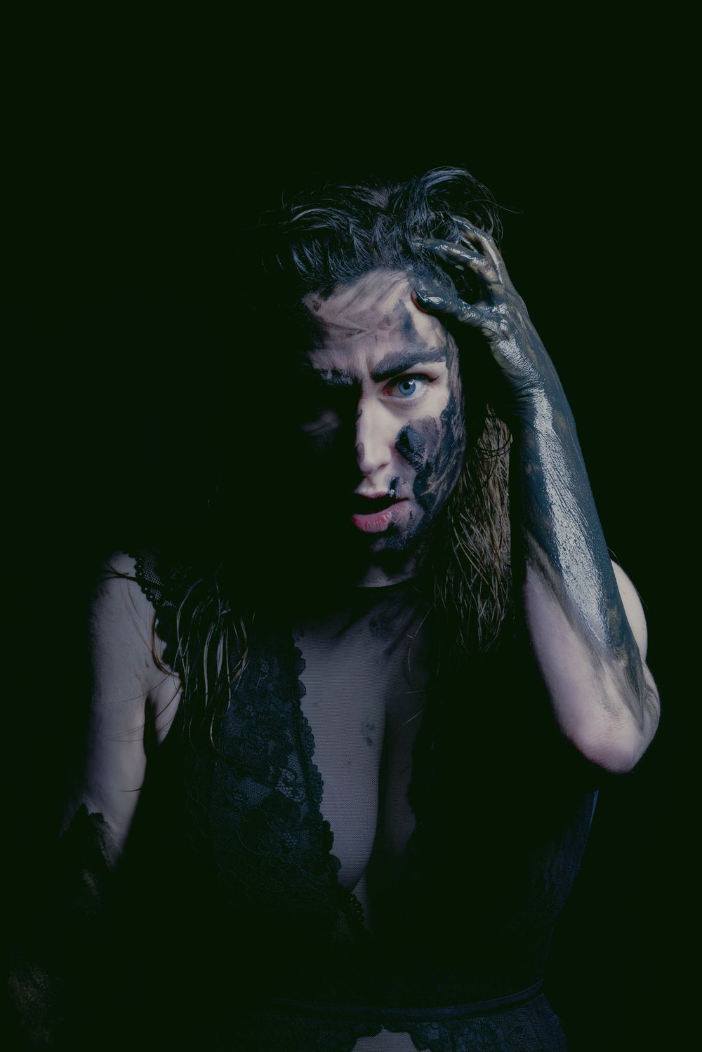 Dark moody portrait with dramatic shadows and long hair against black background.