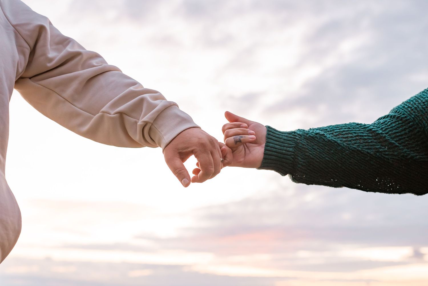 Two people holding hands against a sunset sky, creating a tender moment of connection.