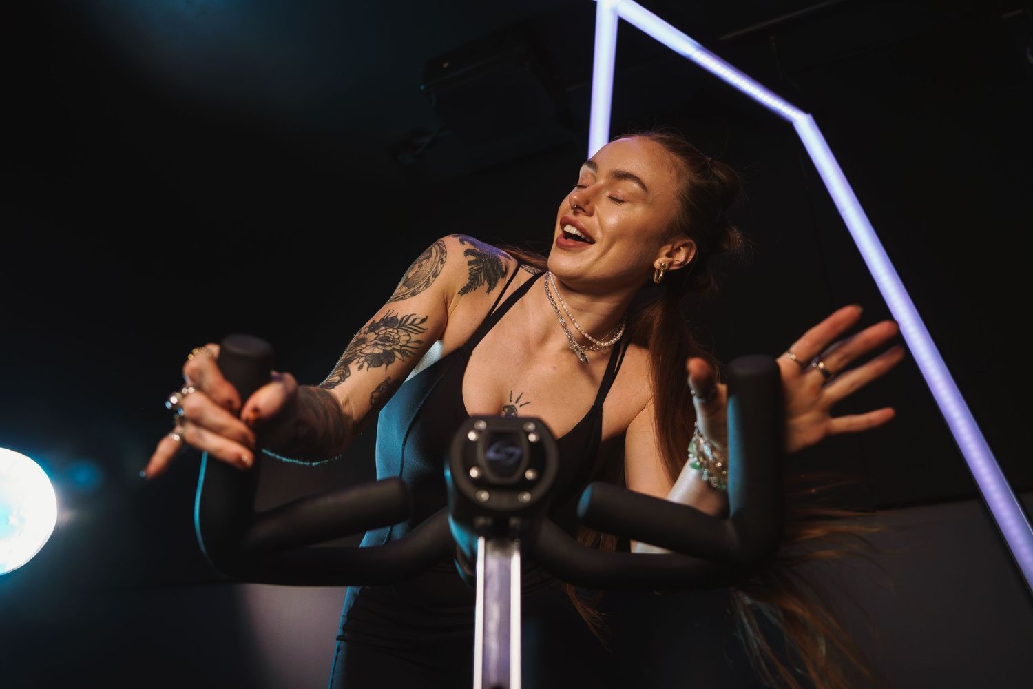 Energetic fitness instructor leading a high-intensity cycling class in a dimly lit studio.