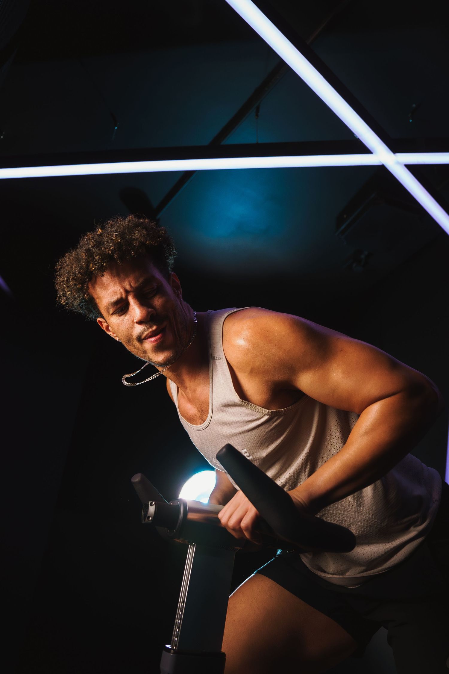 Cyclist in tank top working out intensely on stationary bike under dramatic lighting.