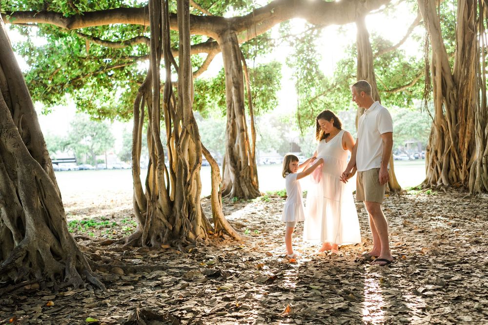 A family stands together under a majestic banyan tree with sunlight streaming through the branches.