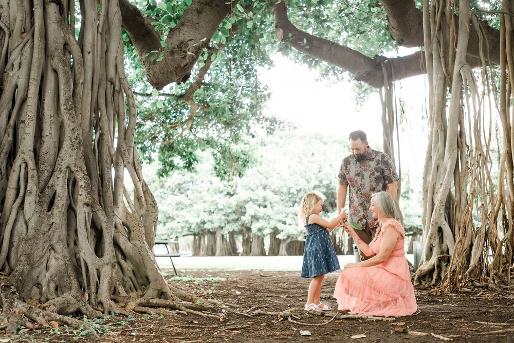 A couple poses under a large banyan tree with cascading aerial roots and lush green canopy in a park setting.