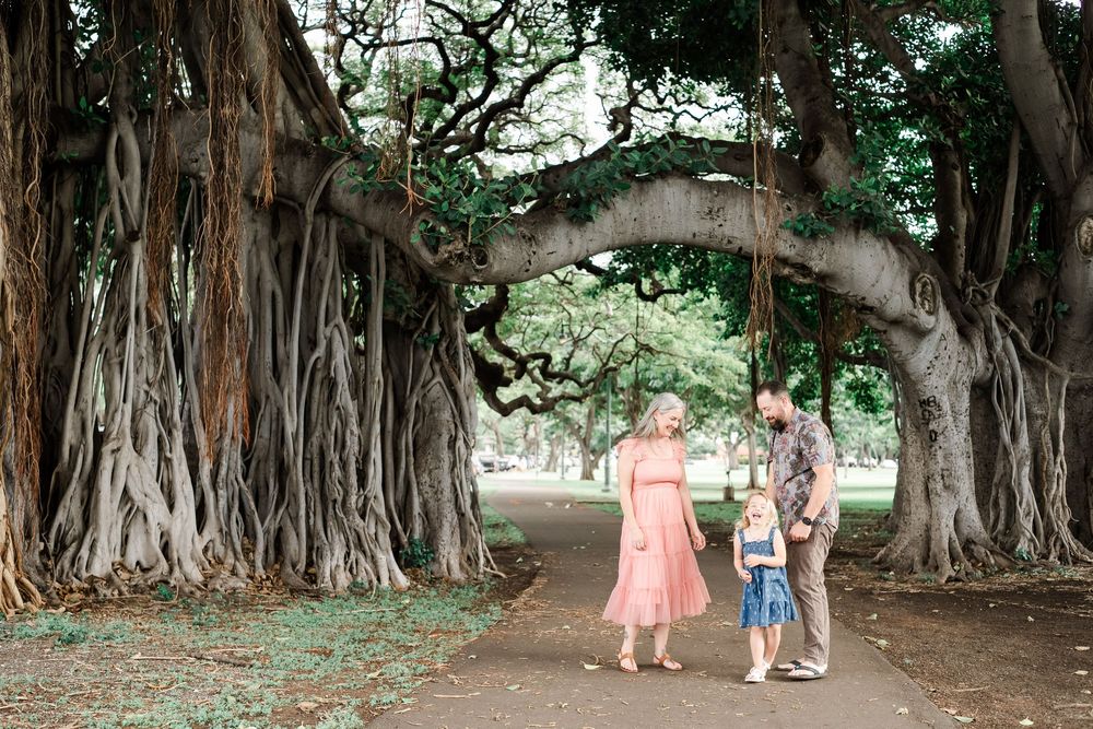 Family walking beneath majestic banyan trees with hanging aerial roots on a path in a tropical garden.