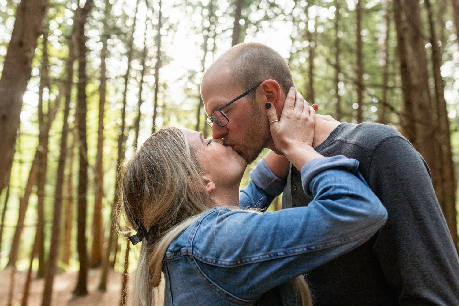 Romantic couple embracing among tall pine trees in a forest setting.