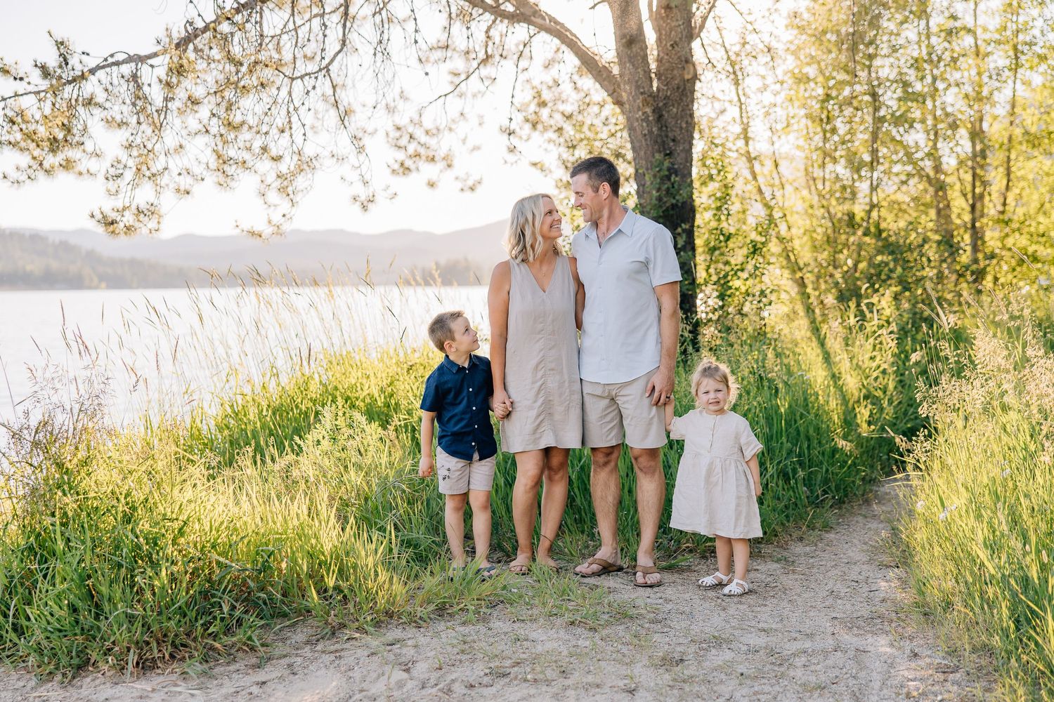 Family standing together on a nature path beside a serene lake at sunset.