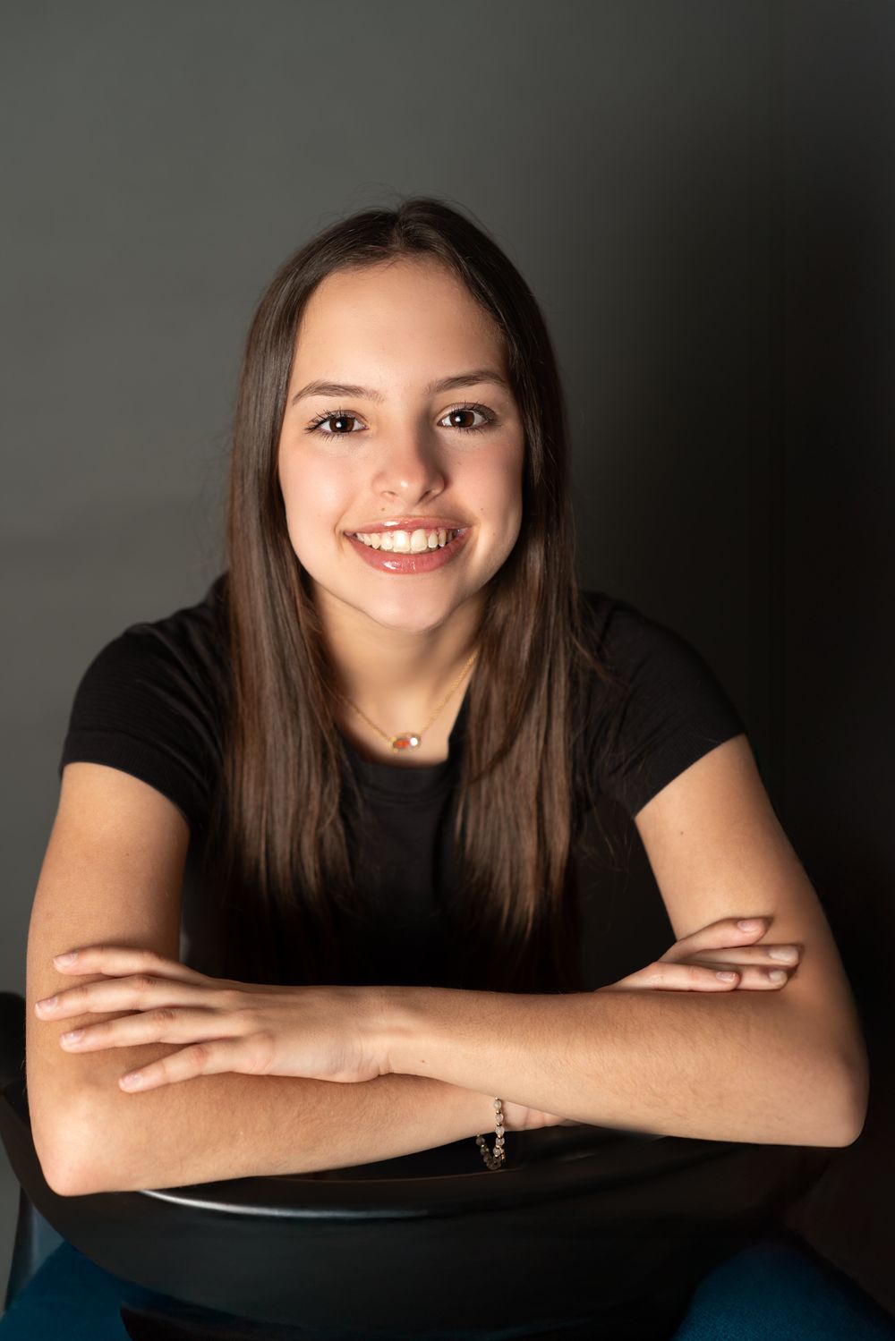 A young tween sitting in a chair for a headshot with a black shirt on