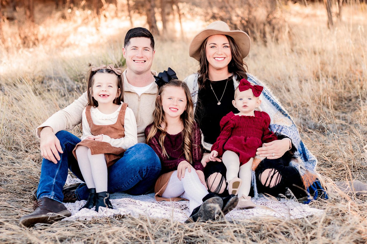 Family portrait in casual attire sitting together on blanket in golden autumn field at sunset.