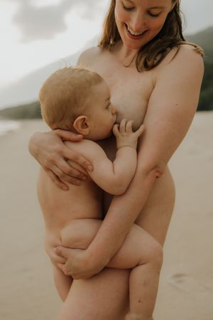 A tender moment of nursing between parent and infant captured on a serene beach.
