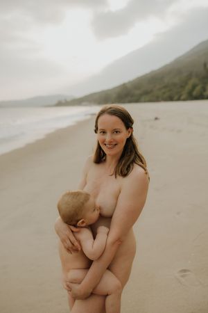 A tender moment between parent and baby is captured on a misty beach with mountains in the background.