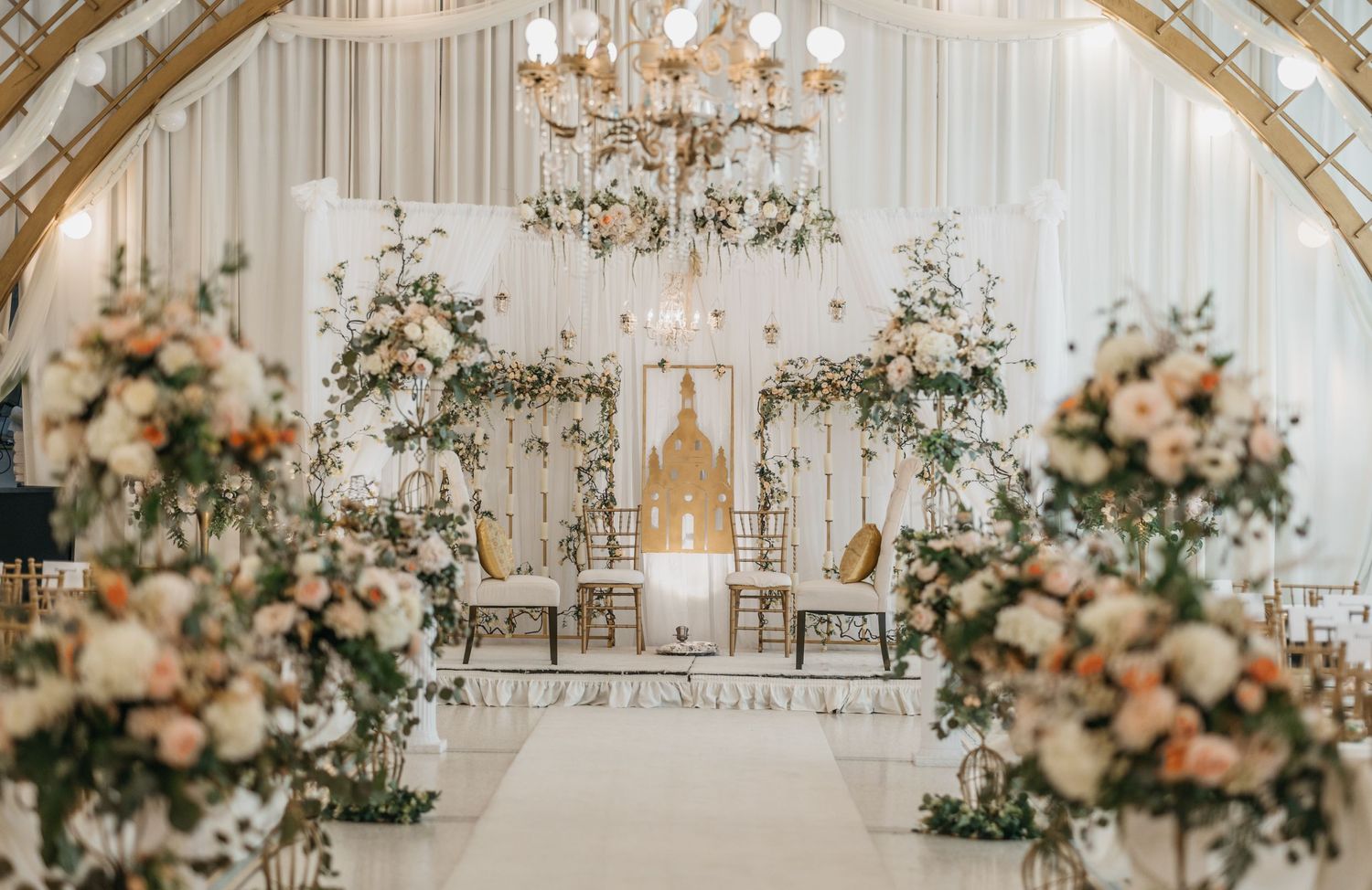 Elegant white wedding ceremony setup with chandelier and floral arrangements creating an aisle.