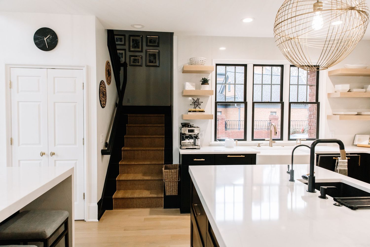 Modern kitchen with black island, white quartz countertop, rattan pendant light, and open shelving.
