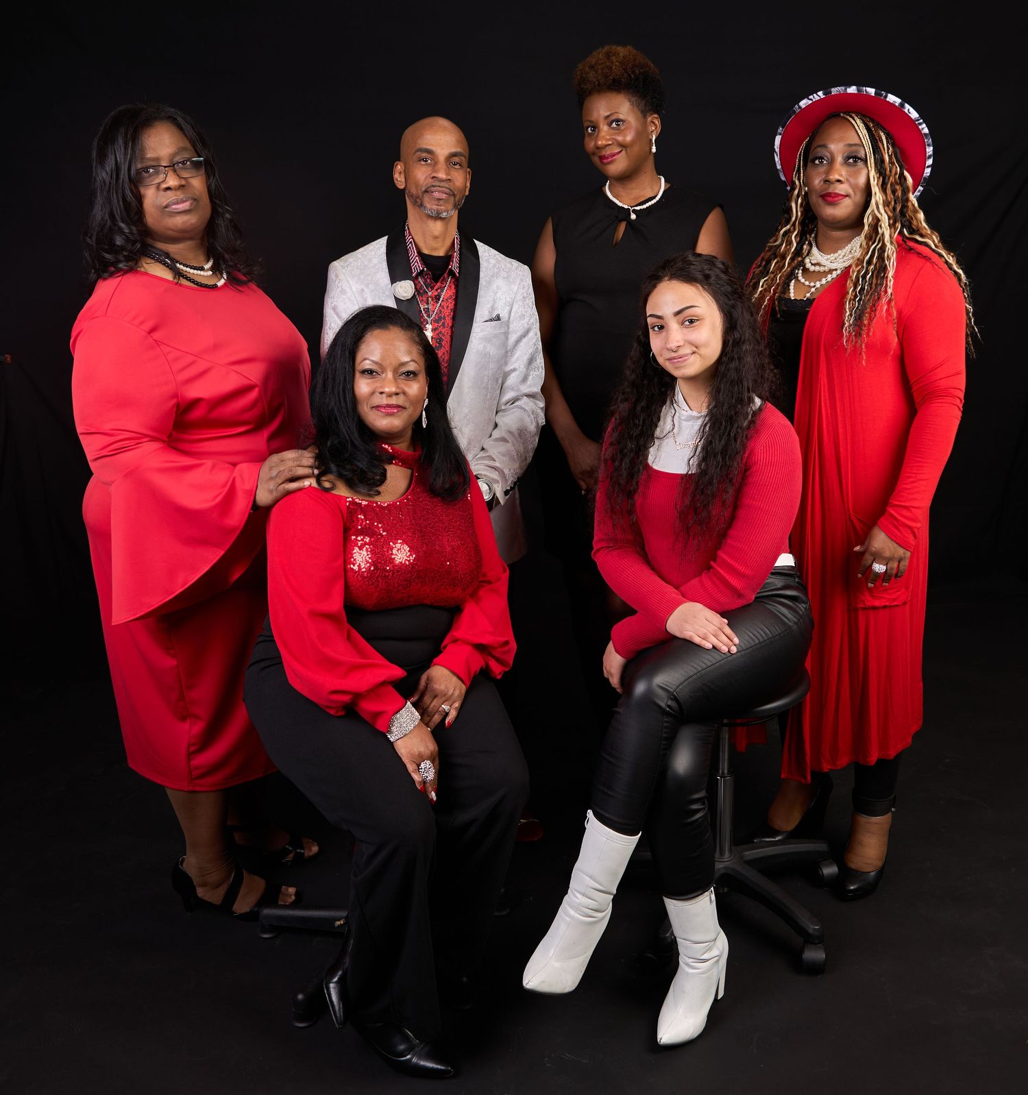 Professional photo shoot with group in red and black formal attire against dark background.