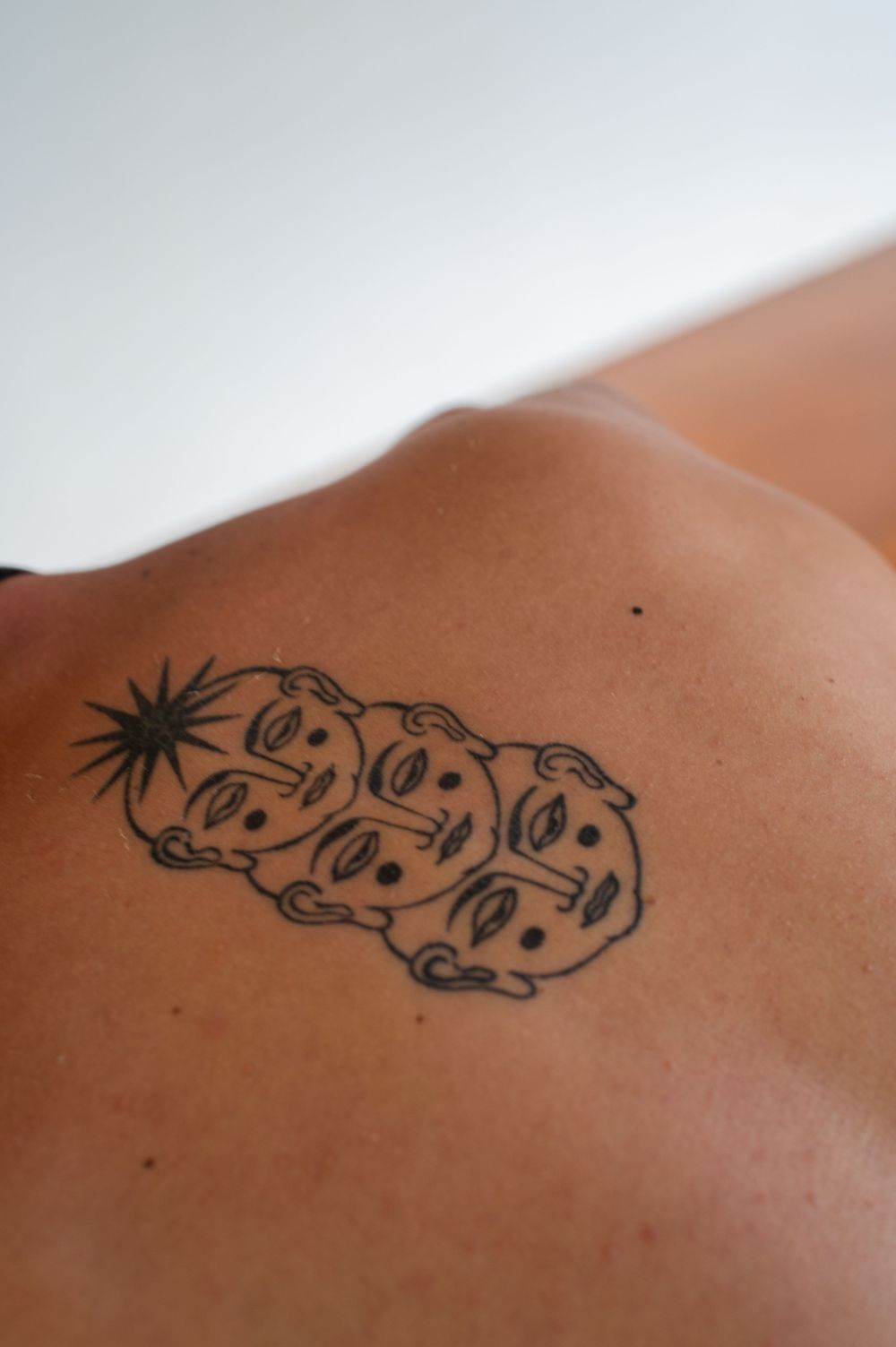 Photo of man's upper back / lower neck tattoo of three faces