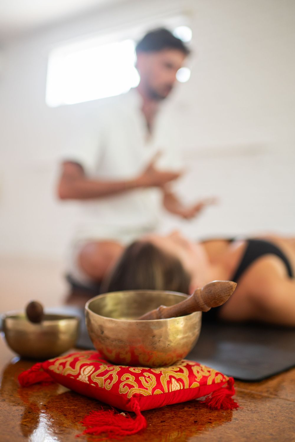 Woman doing sound meditation with yoga teacher next to her. Sound bowls are at the front of the image.