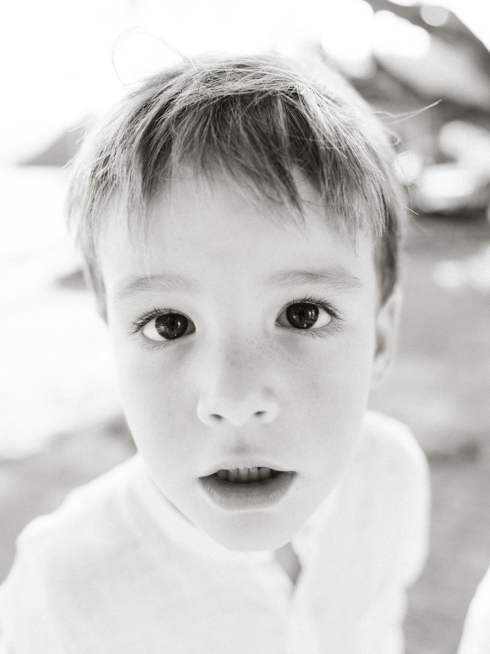 Black and white portrait of a young boy with short hair looking up at the camera with wide curious eyes.