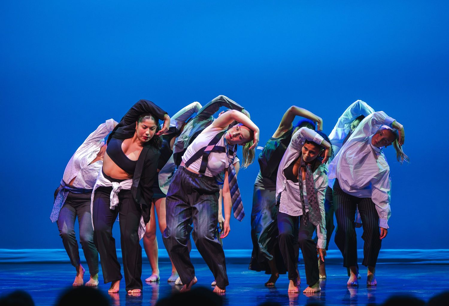 Contemporary dancers perform synchronized movements on stage with blue lighting.