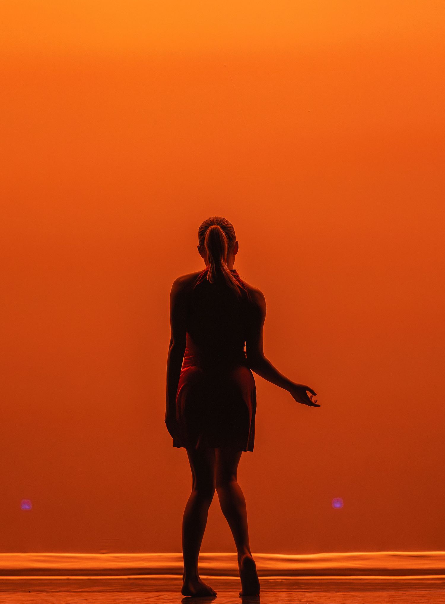Silhouette of performer against dramatic orange backdrop on stage.