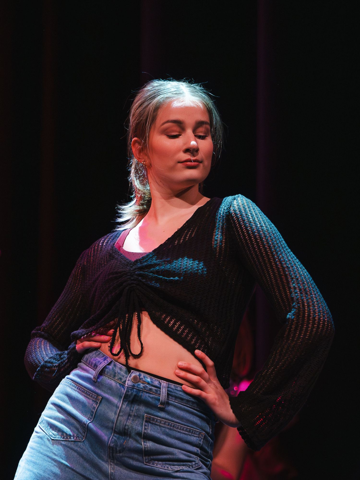 Stage performance featuring cropped sweater and denim in dramatic lighting.